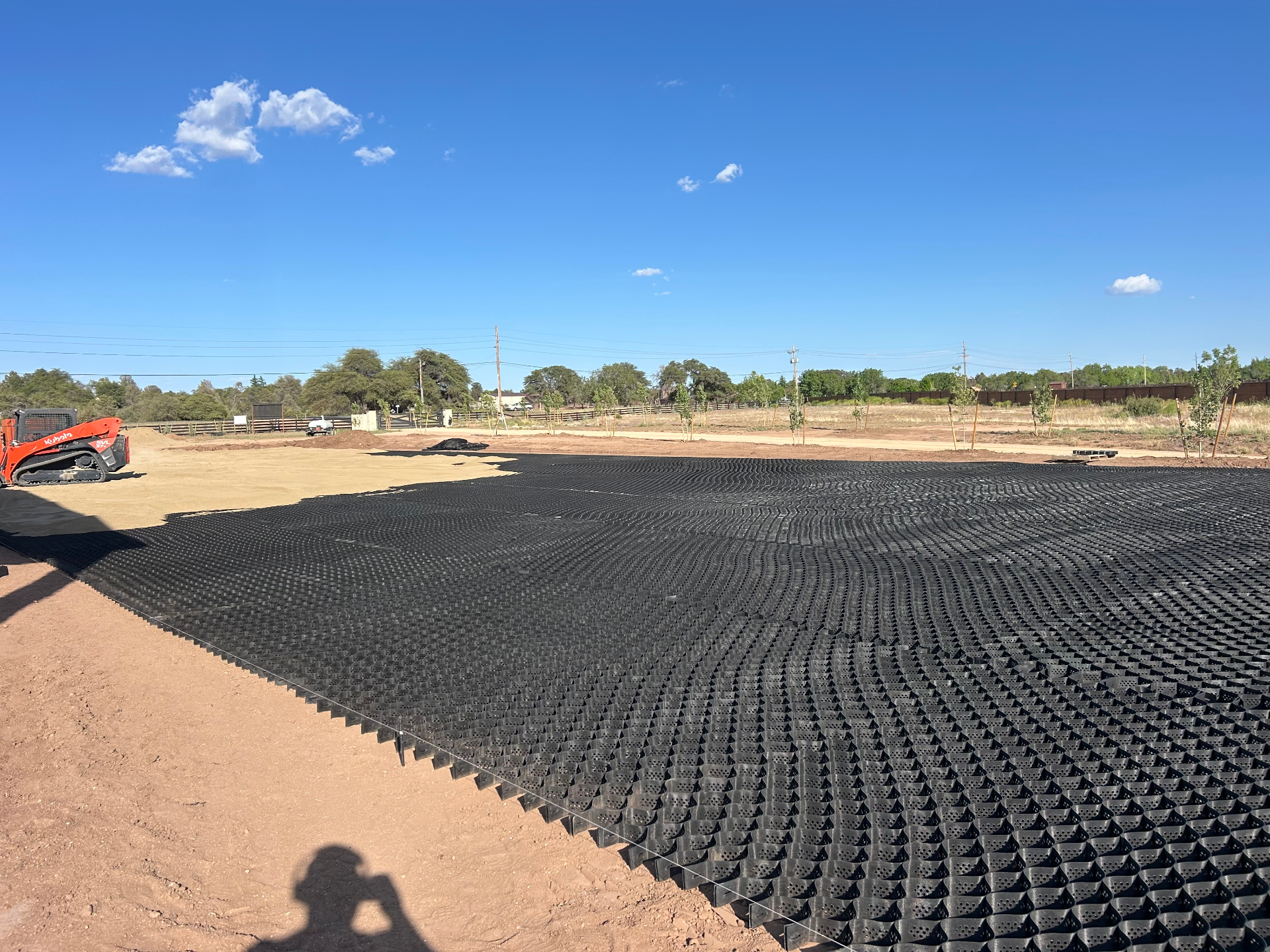 Prescott AZ Geocell Arena Pad Geocell grid laid across a graded outdoor arena pad in Prescott, Arizona with skid steer and tree line in background